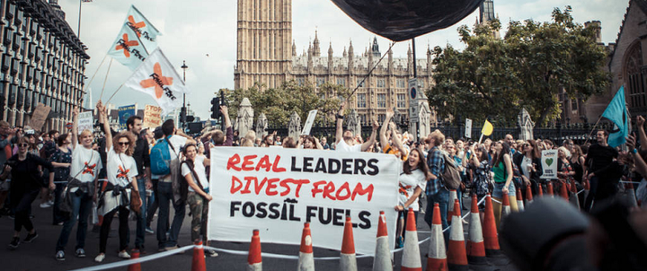 Photo of protesters outside the houses of Parliament in the UK, holding a sign that says 'Real leaders divest from fossil fuels'